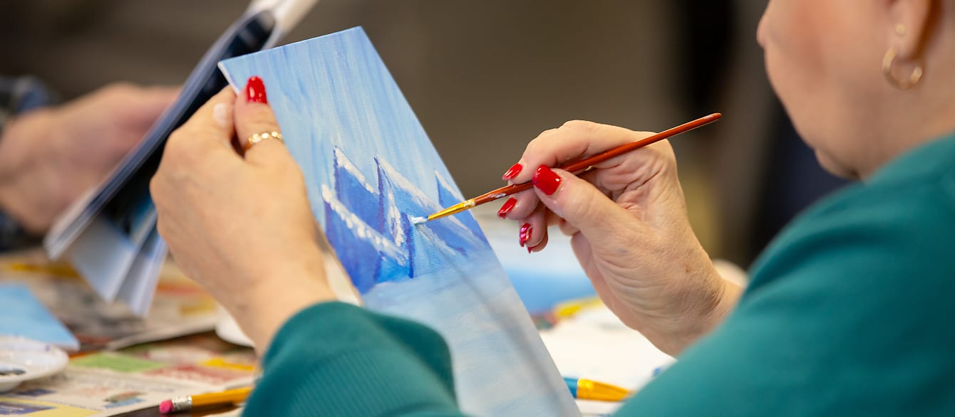Close-up of a woman painting a blue mountain scene