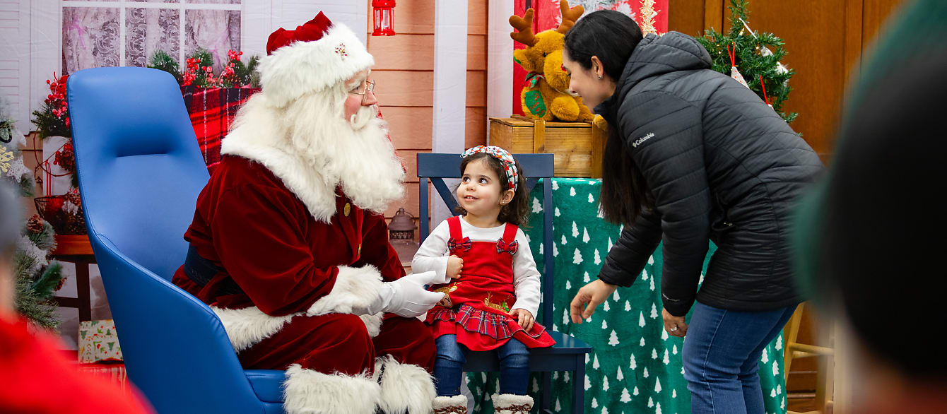Santa sits in a chair and shares a word with a mom as she gets her infant daughter settled in the seat beside Santa.