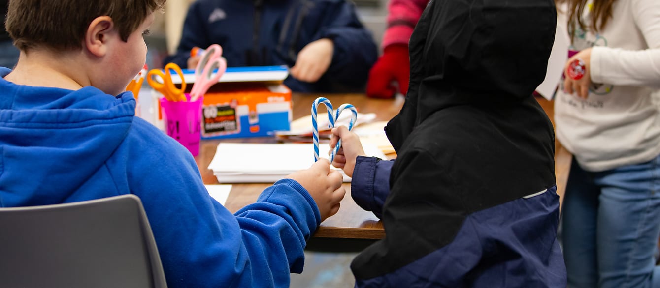 Two young boys place their blue candy canes together to create a heart shape.