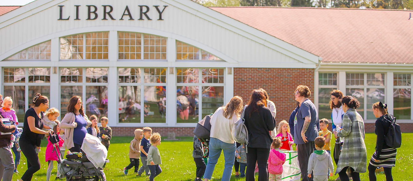 A large group of people ranging from parents to babies in strollers gather outside the library to release butterflies.