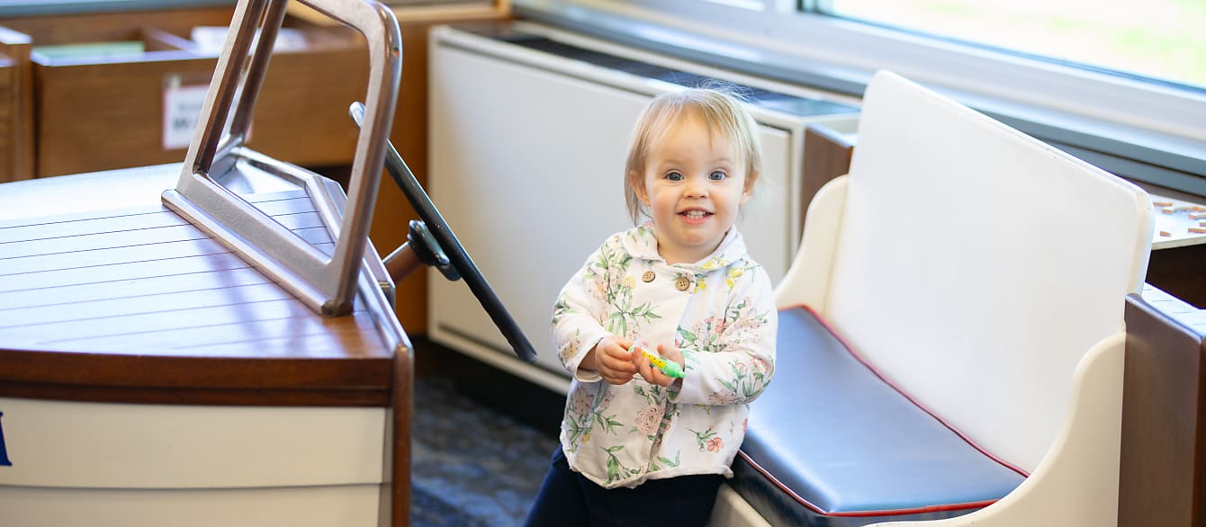 A female toddler with short blonde hair in a flowery raincoat flashes the camera a huge, toothy grin.
