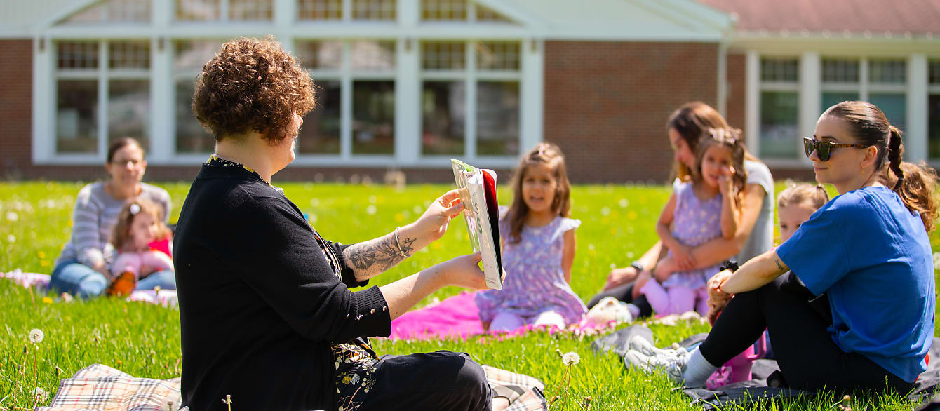 A librarian shows a crowd of parents and children on picnic blankets a page from a picture book.
