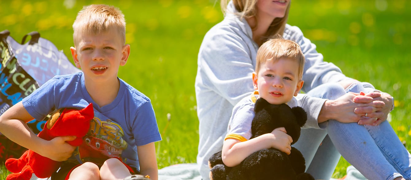 Two brothers sit on a picnic blanket holding their teddy bears while listening to a story.