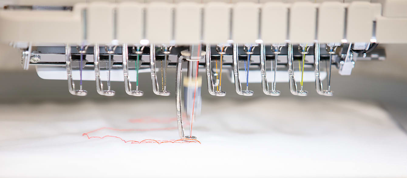 A close-up of the embroidery machine in the Create Space while it is on. Multicolored thread is looped through ten needles.
