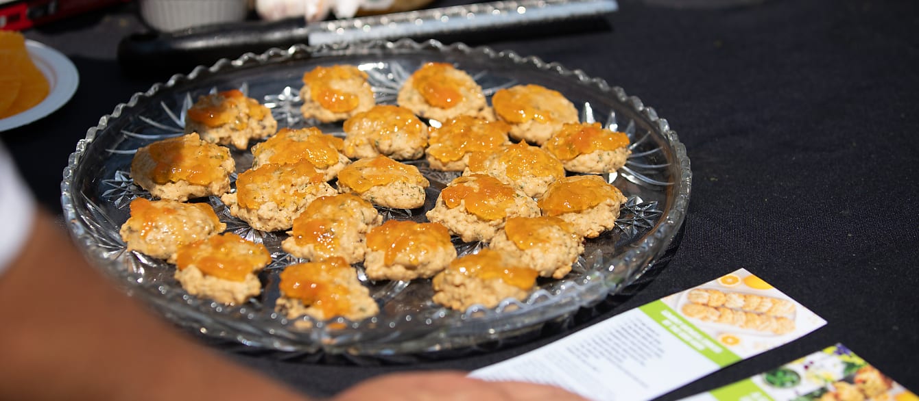 A large plate of cookies covered in apricot jam sits on a black table next to some recipe cards.