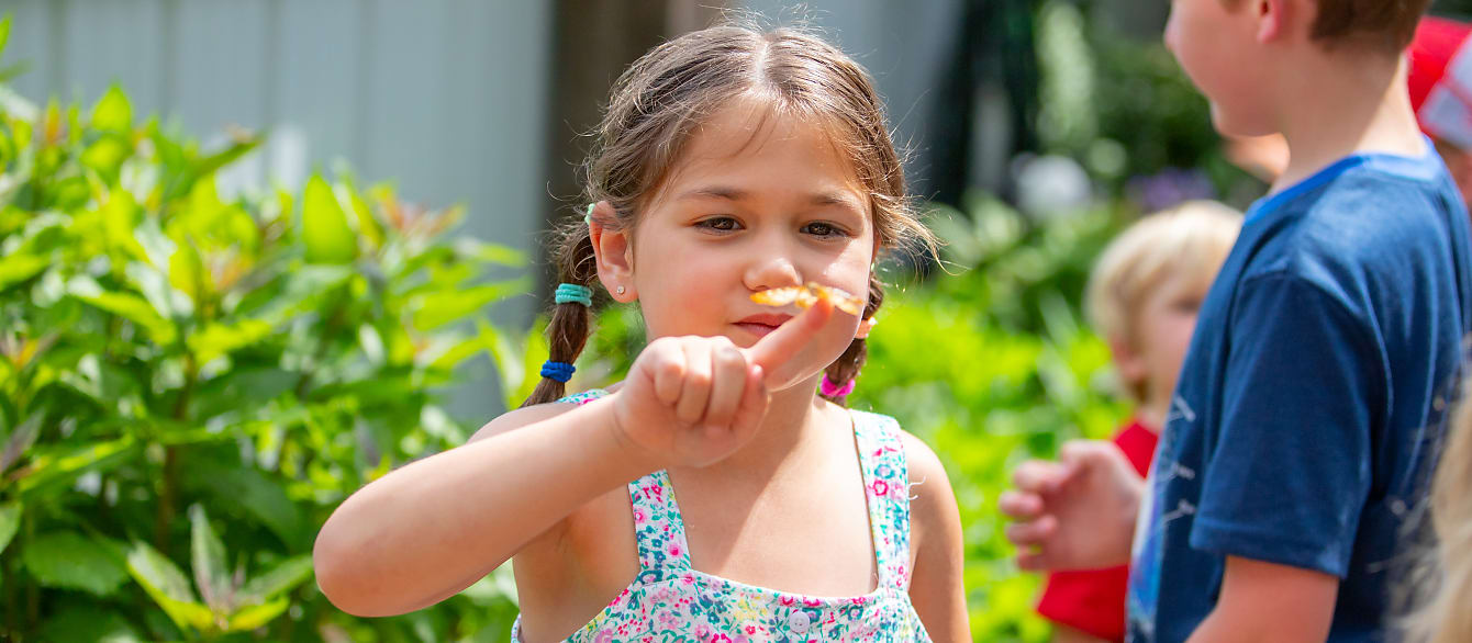 A school-age girl with dark hair in two braids holds a small butterfly on her finger.