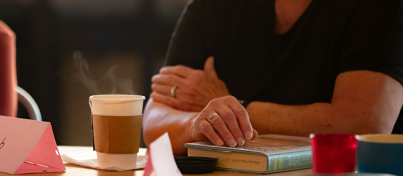 A close-up of a to-go coffee cup with steam above it sitting on a table next to a library book