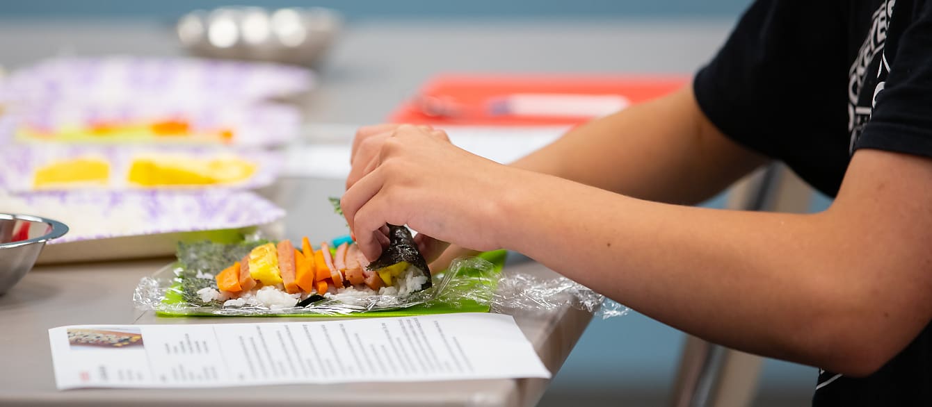 Close-up photo of a teenager learning to roll Korean Gimbap