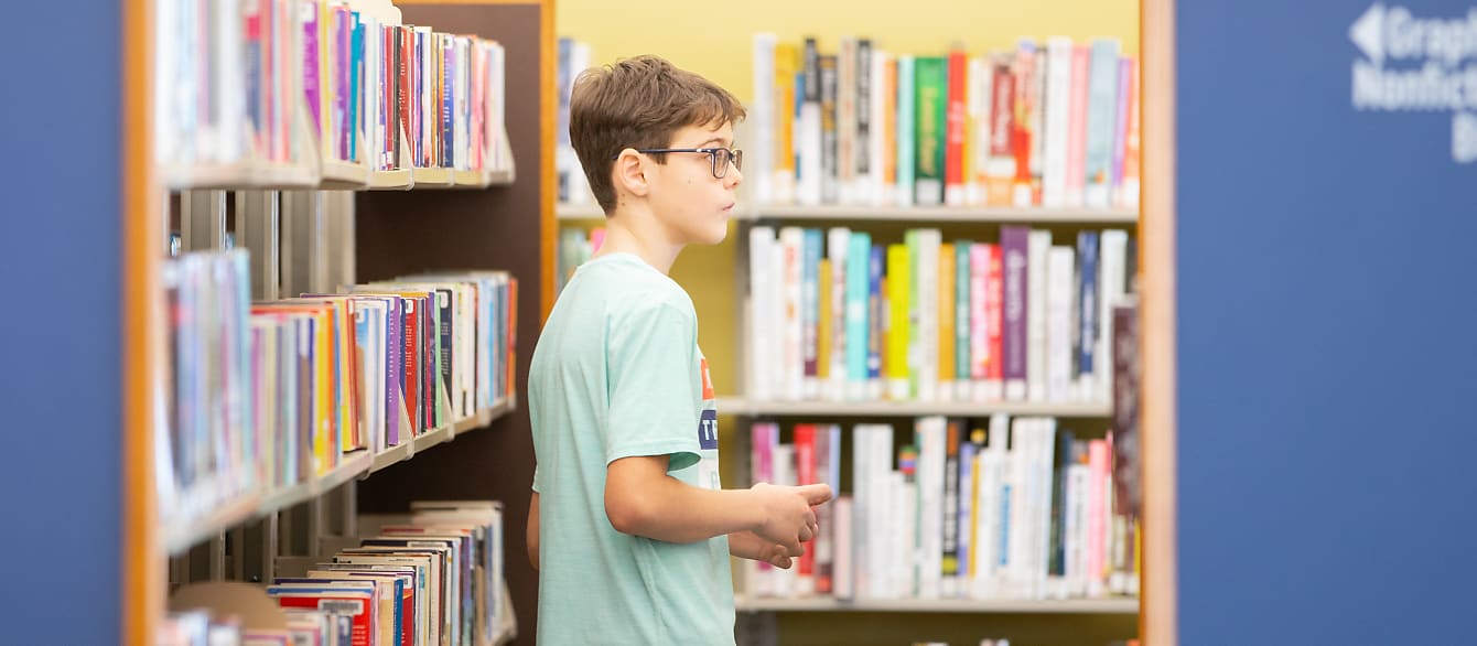 A young boy wanders aisles of books in search of something specific.