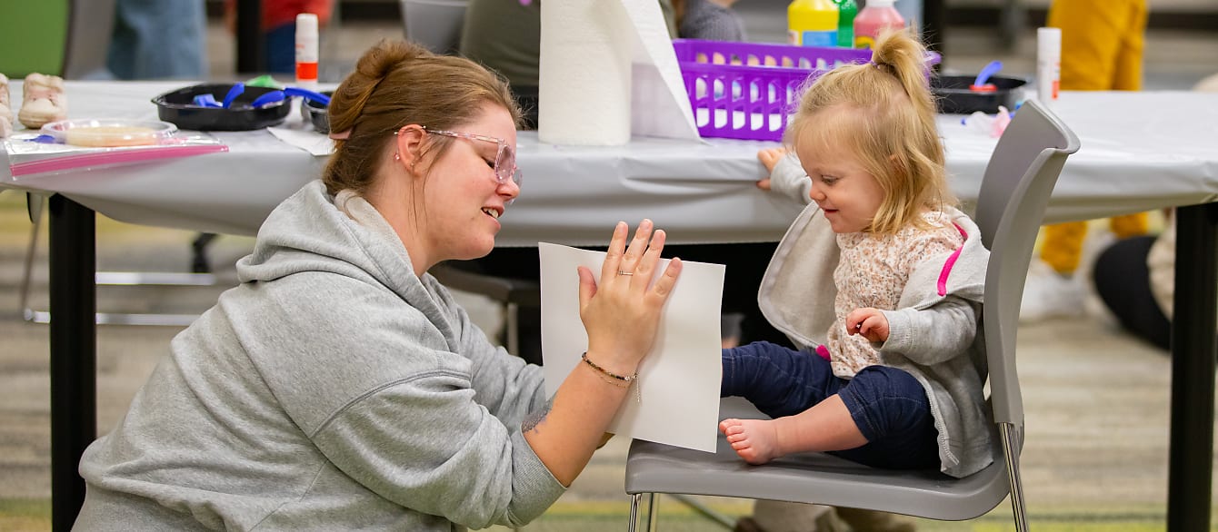 A mom sitting on the ground stamps her baby's painted foot on a piece of paper.