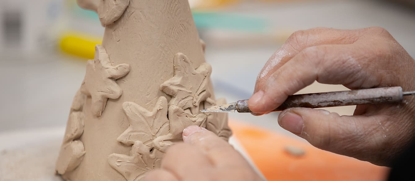 A close-up of someone carving clay leaves into a cone shape.