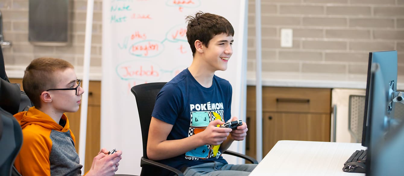 A teen boy cheers at a computer screen with a controller in his hands.