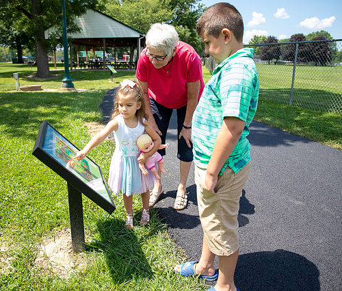 Image of Grandmother and 2 Grandchildren looking at a StoryWalk&reg; Book
