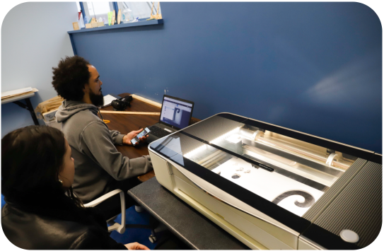 Two people working next to a laser cutter