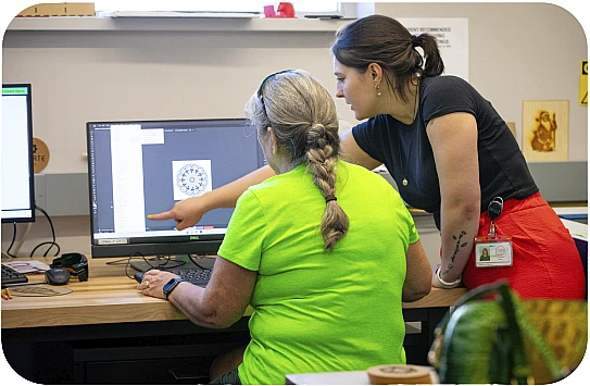 A Library Employee helping a patron design at a computer.